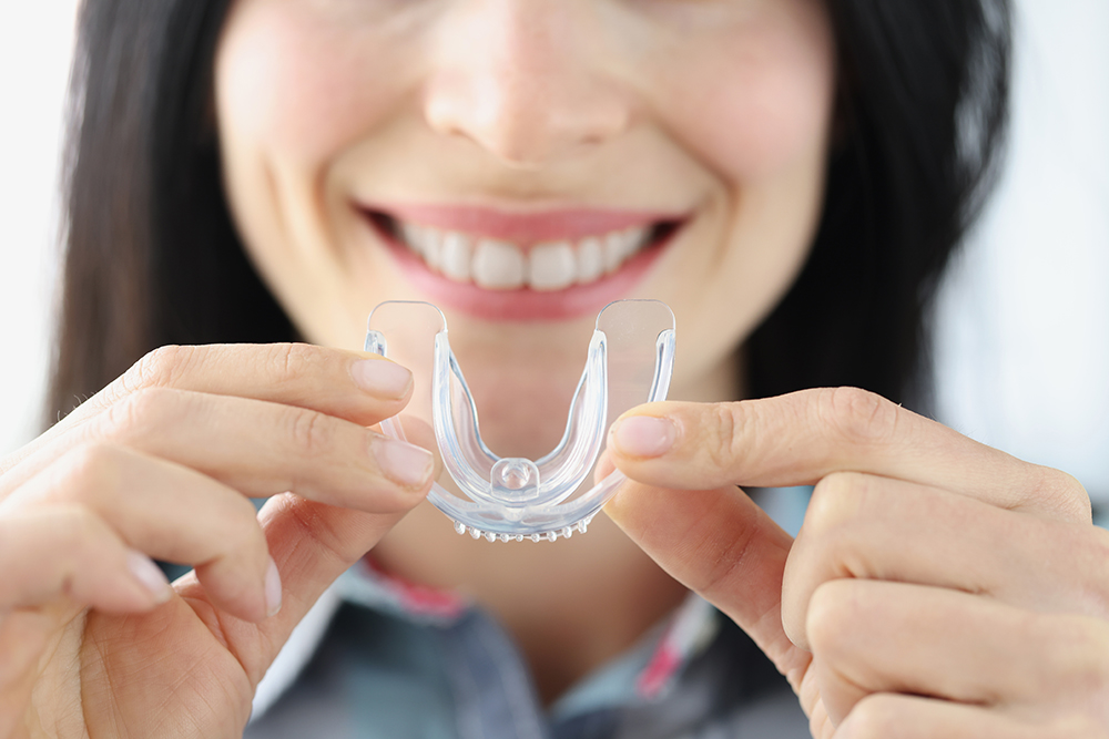 Woman holding plastic mouth guard for bruxism treatment closeup